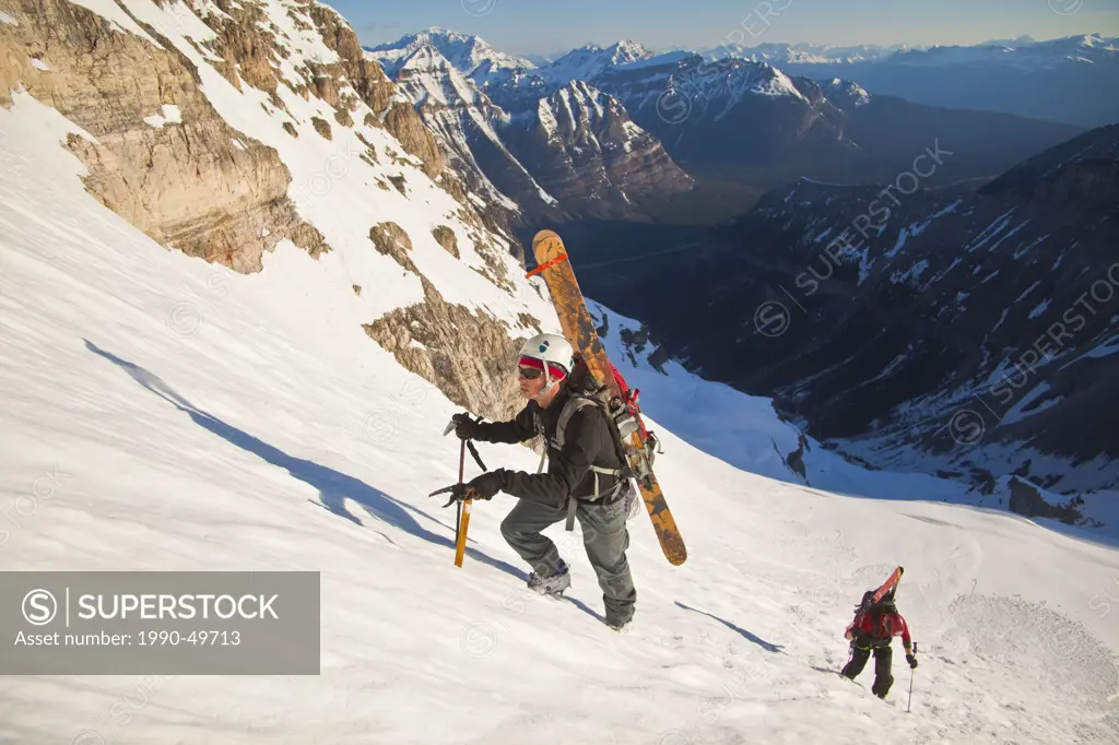 Two male backcountry skiers bootpack up a steep face of the North Face of Mt. Stanley, Kootenay National Park, British Columbia, Canada