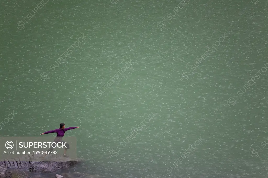 A woman does yoga in the rain at Medicine Lake Jasper National Park, Alberta, Canada