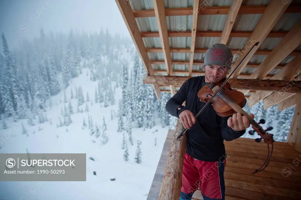 A man takes a break from backcountry skiing to make some music. Icefall Lodge, Golden, British Columbia, Canada