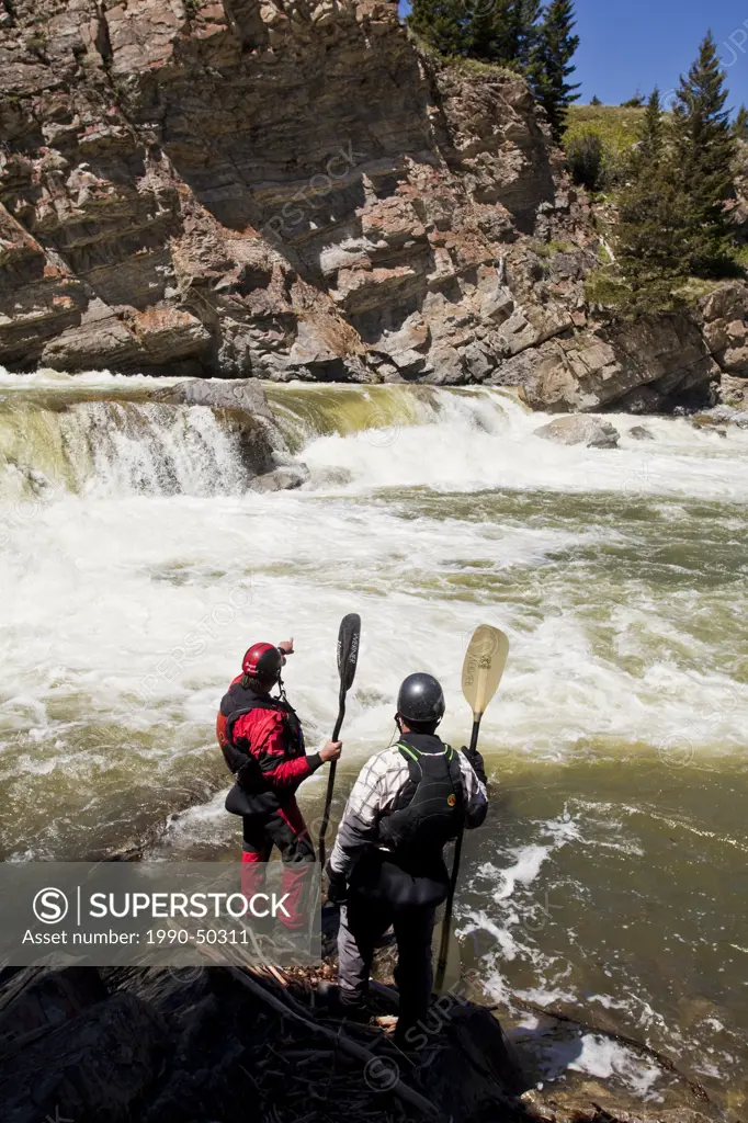 Two male whitewater kayakers scout the falls on the Oldman River, Alberta, Canada