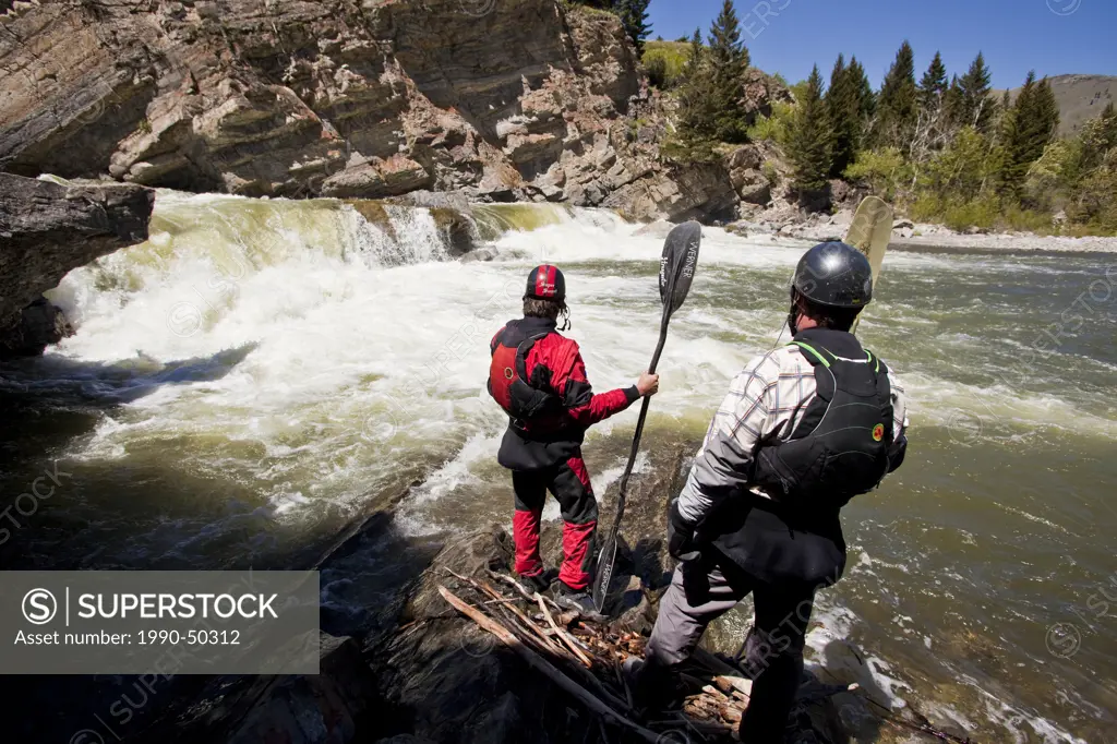 Two male whitewater kayakers scout the falls on the Oldman River, Alberta, Canada