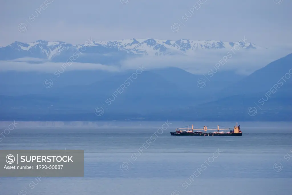 A freighter passes through the Starit of Juan de Fuca with the Olympic Mountains in the background, British Columbia, Canada.