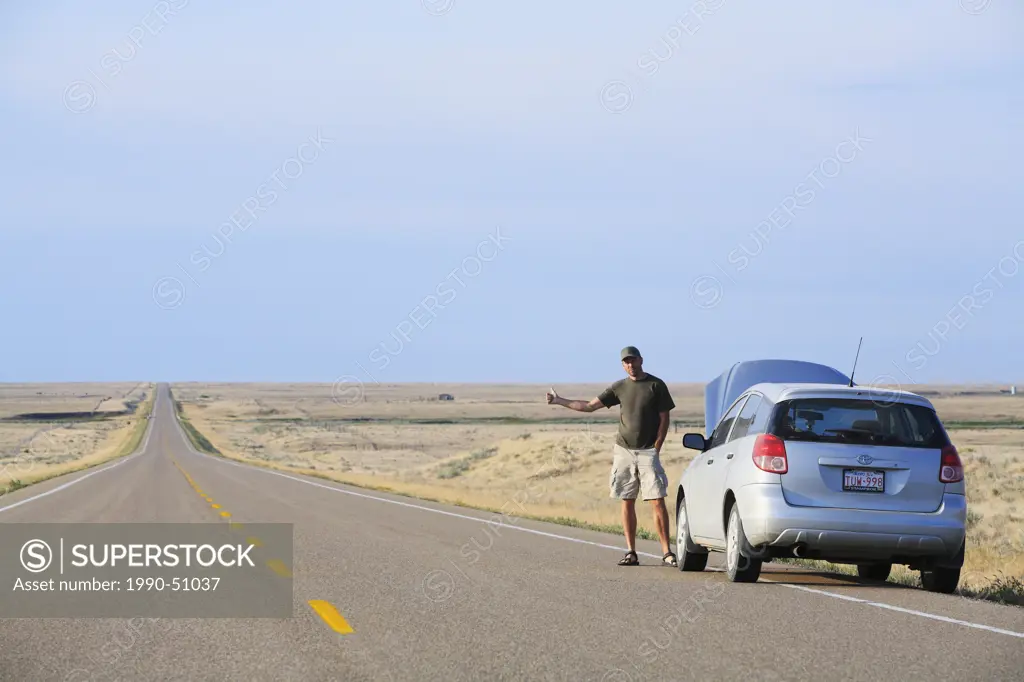 Man hitchhiking on a deserted prairie road after his car breaks down, Alberta, Canada