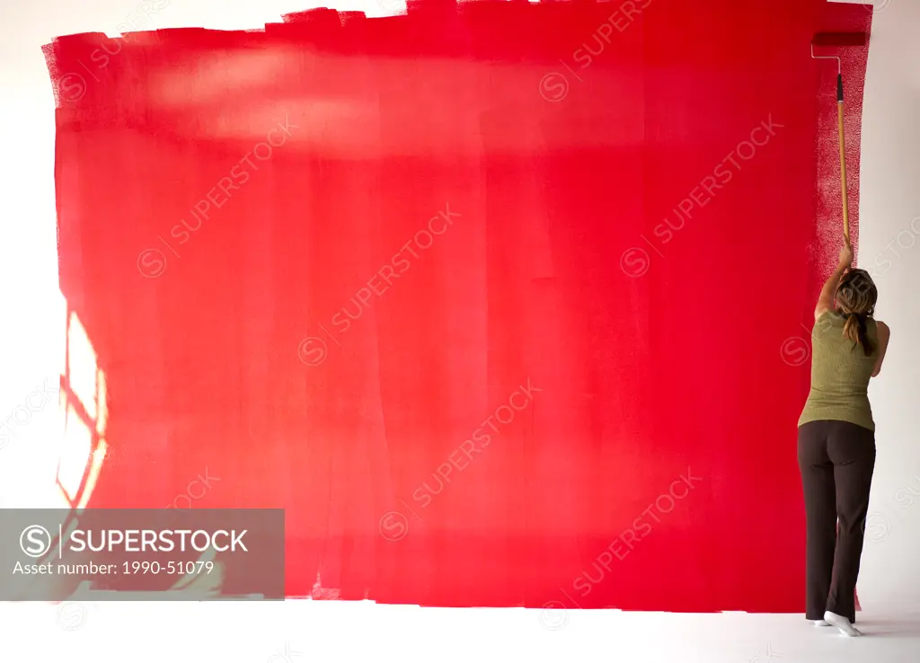 31 year old Italian woman painting red on a white wall in a loft, Montreal, Quebec, Canada.