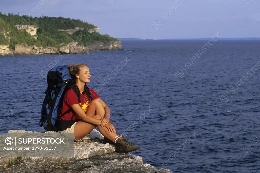 A young woman backpacker rests on an overlook of the Niagara Escarpment along the Bruce Trail, Bruce Peninsula National Park, Ontario, Canada.