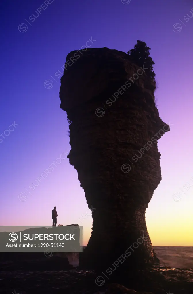person standing next to the flowerpot rock formatiom at sunrise, Fathom Five National Marine Park, Ontario, Canada.