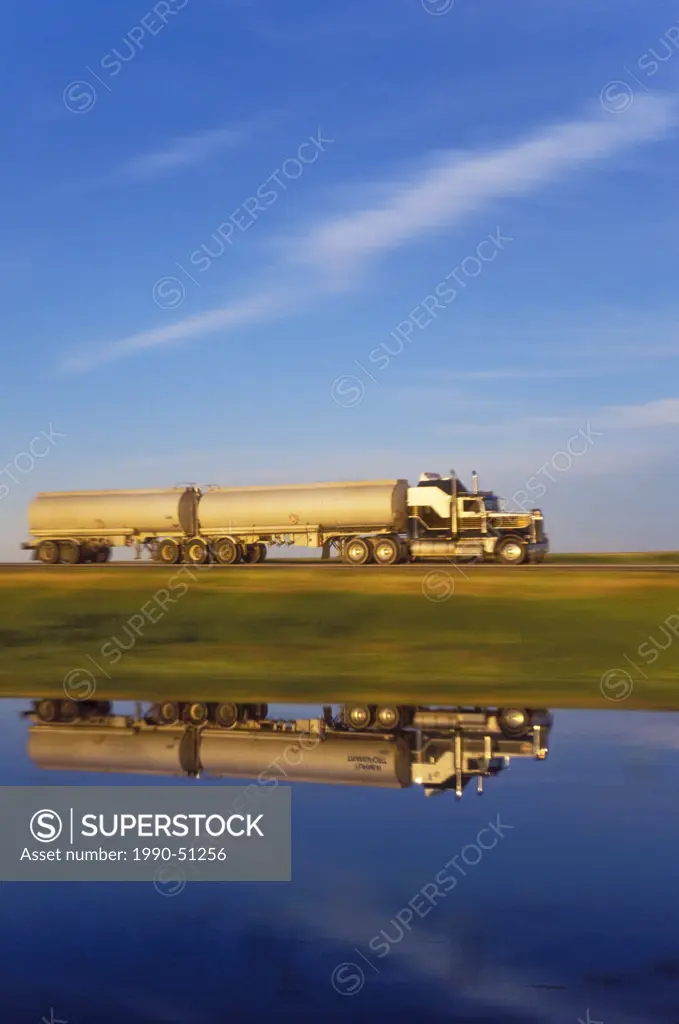 Transport truck casts reflection in pond as it carries goods across the Canadian Prairies on the Trans_Canada Highway, Saskatchewan, Canada.