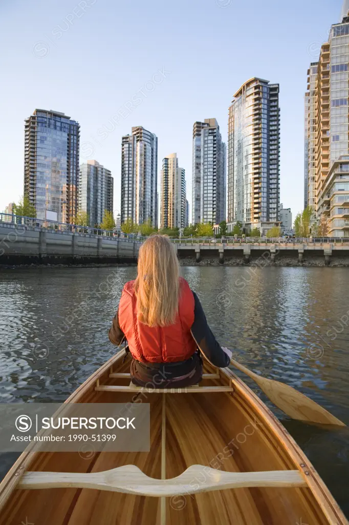 Girl paddling canoe across from downtown condominiums, False Creek, Vancouver, British Columbia, Canada.