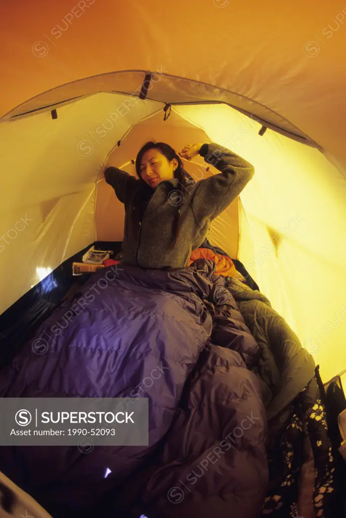 A young woman waking and stretching in a tent in Jasper, Alberta, Canada.