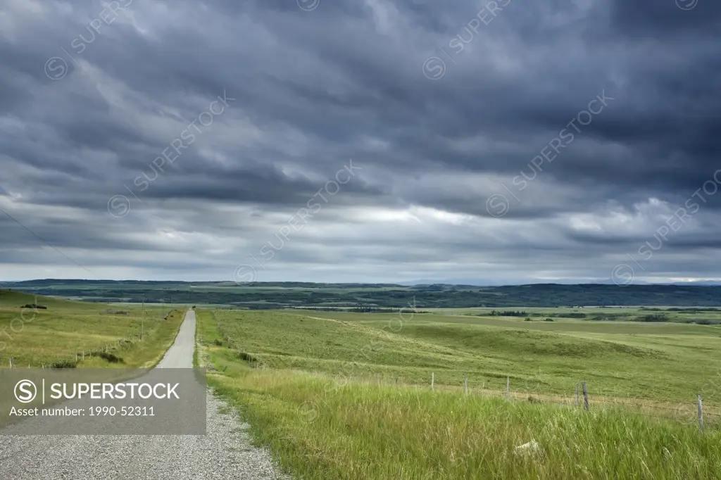 Country road, field, and fence with storm clouds near Cochrane, Alberta, Canada