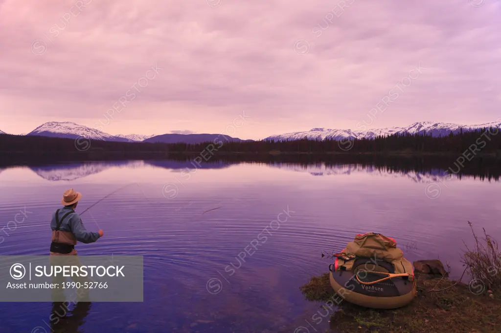 Fly fisherman casting for trout at dawn, McBride Lake near Morice Lake, British Columbia