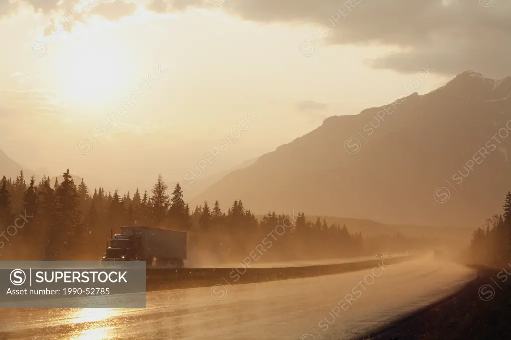 A semi transport truck drives through a dramatic summer rainstorm at sunset along the Trans_Canada Highway in Banff National Park, Alberta, Canada