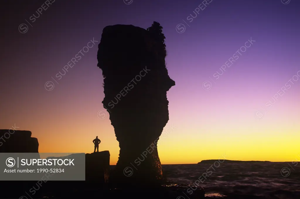 Person standing next to the flowerpot rock formatiom at sunrise, Fathom Five National Marine Park, Ontario, Canada.
