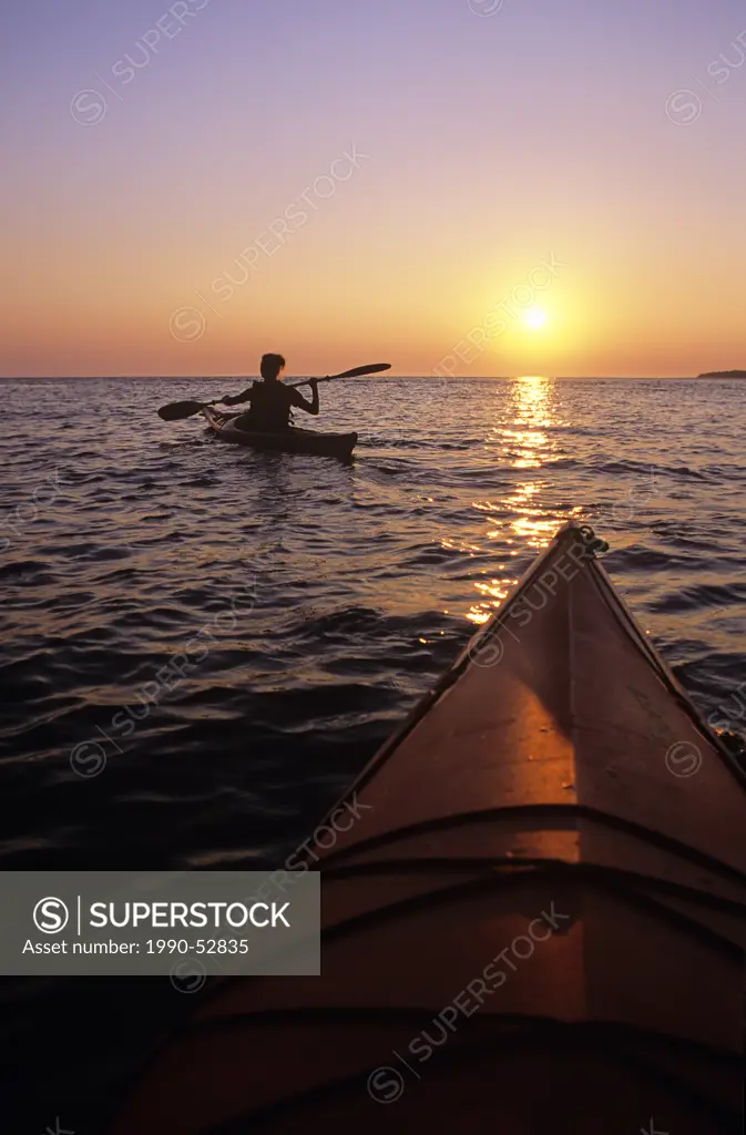A young woman paddles her kayak at sunset along the Lake Huron shoreline, Fathom Five National Marine Park, Ontario, Canada.