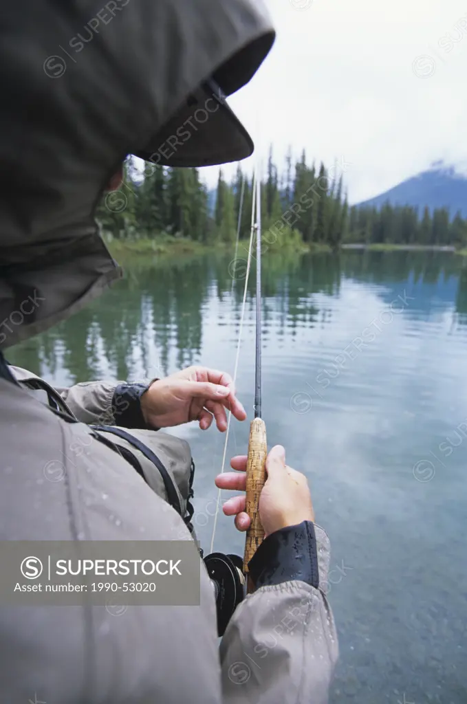Male fly fisher strips line on misty day in river, Canadian Rockies, Alberta, Canada.