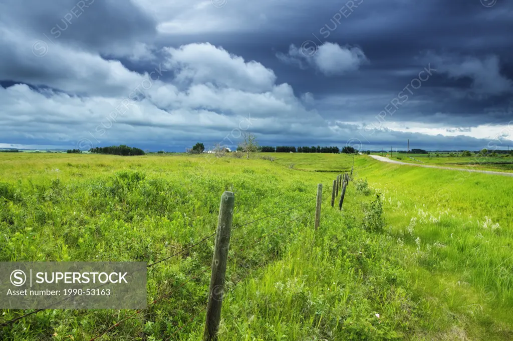 Fence in pasture, country road and stormy sky near Cochrane, Alberta, Canada