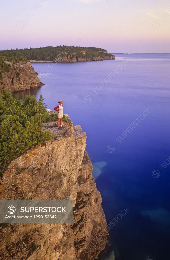 A young woman hiker admires the scenery at sunrise, from an overlook of the Niagara Escarpment along the Bruce Trail, Bruce Peninsula National Park, O...