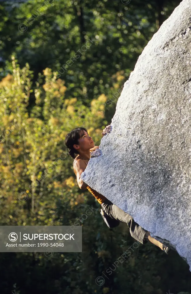Female bouldering on Cutting Edge, V4, Apron Boulders, Squamish, British Columbia, Canada.