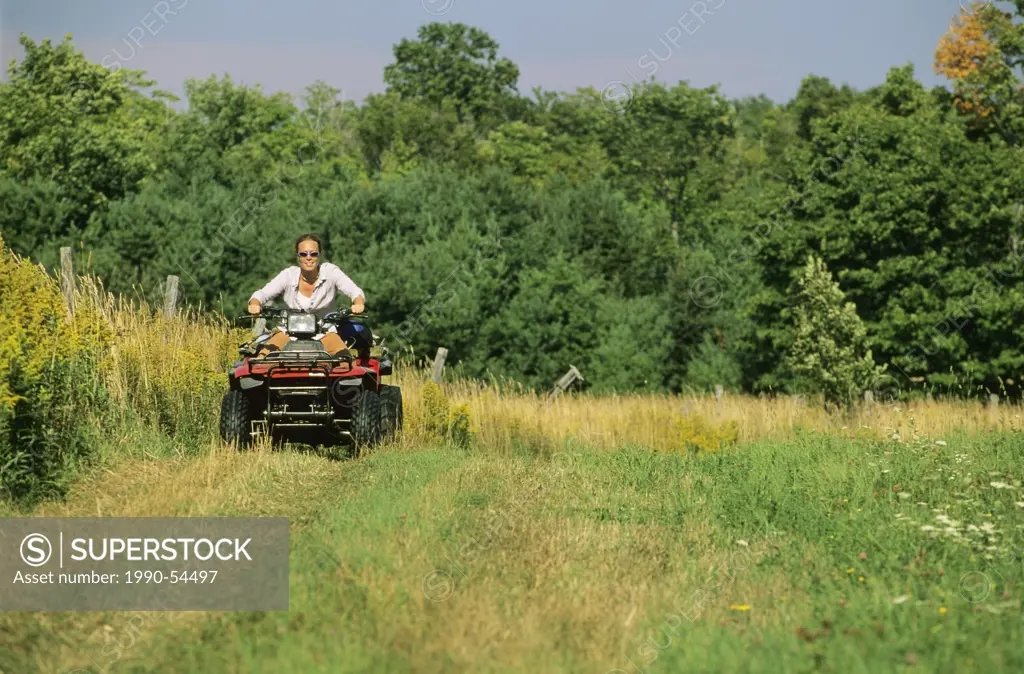 Woman rides a quad ATV on a farm, Manitoulin Island, Ontario, Canada.