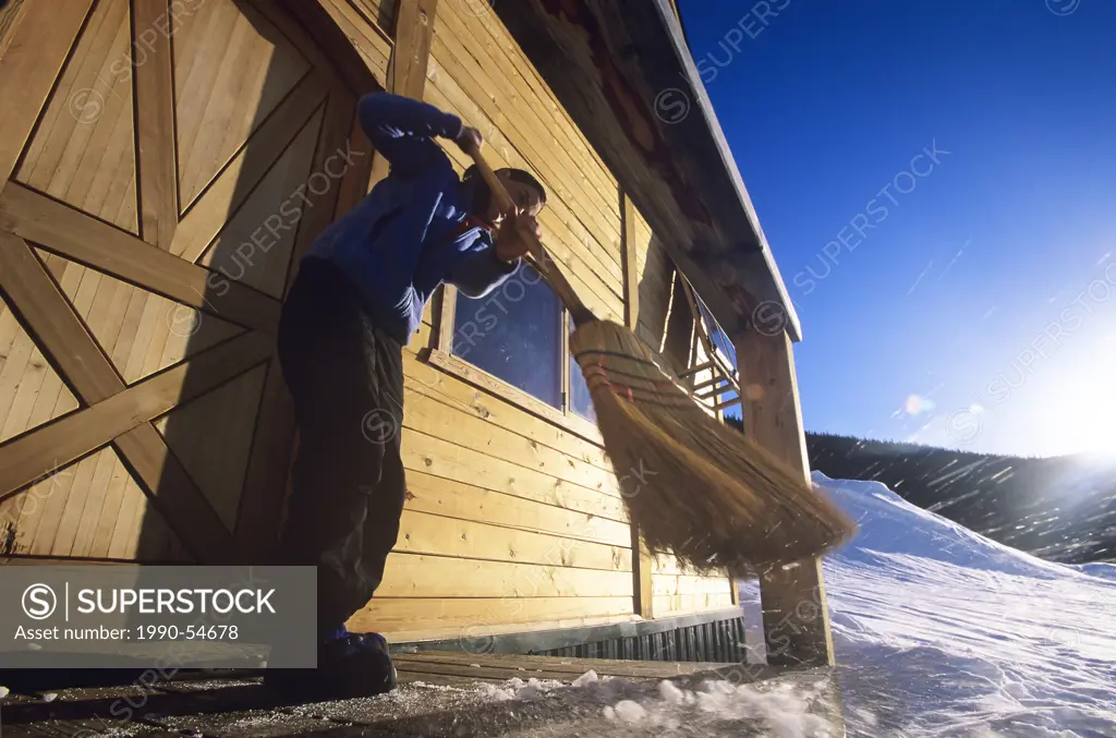 A skier sweeps the deck of an alpine ski cabin, Spring cleaning, The Burnie Glacier chalet near Smithers, British Columbia, Canada.