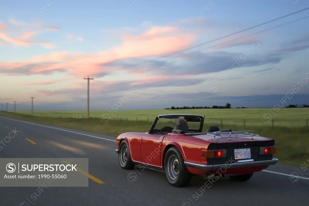 Woman driving red sports car on rural highway, High River, Alberta, Canada.