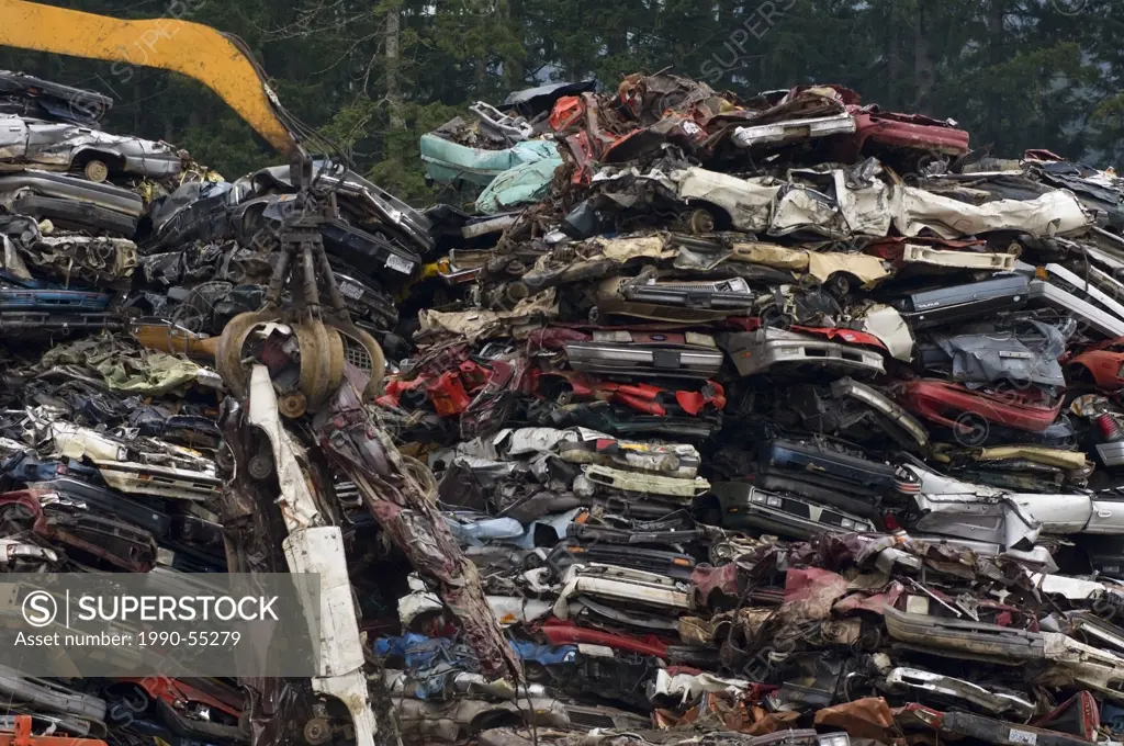Crane lifting flattened cars out of stack of obsolete cars in recycling yard, Vancouver Island, British Columbia, Canada