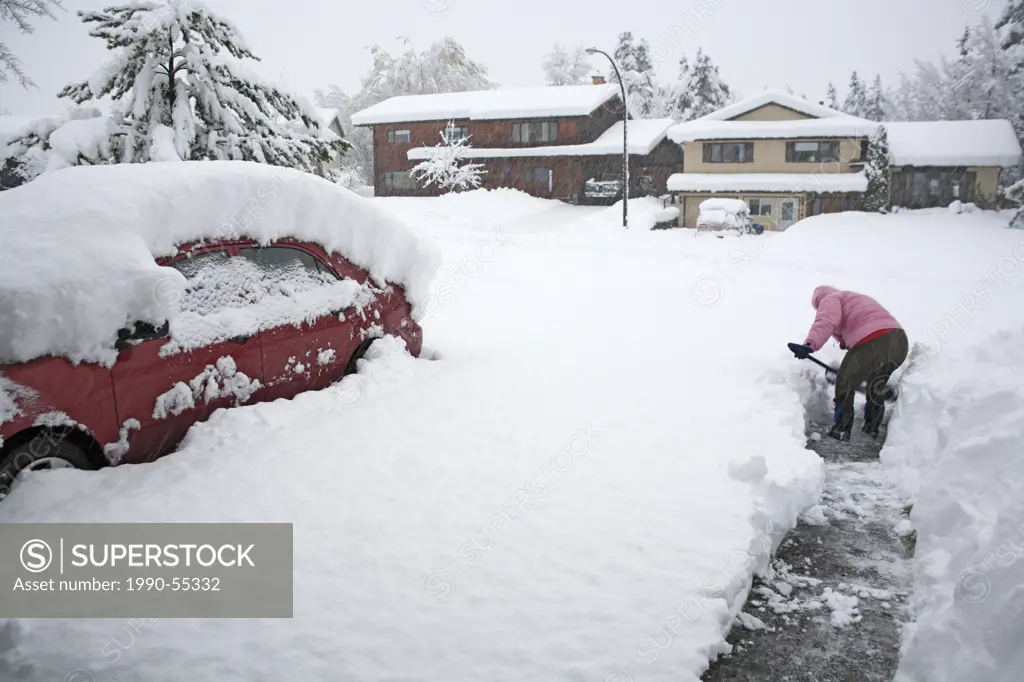 Lady shovelling driveway in snowstorm, Smithers, British Columbia, Canada.