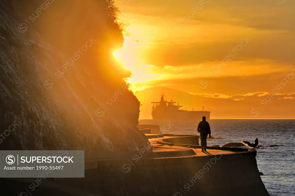 Silhouette of person strolling on the Stanley Park seawall at sunset, Vancouver, British Columbia, Canada