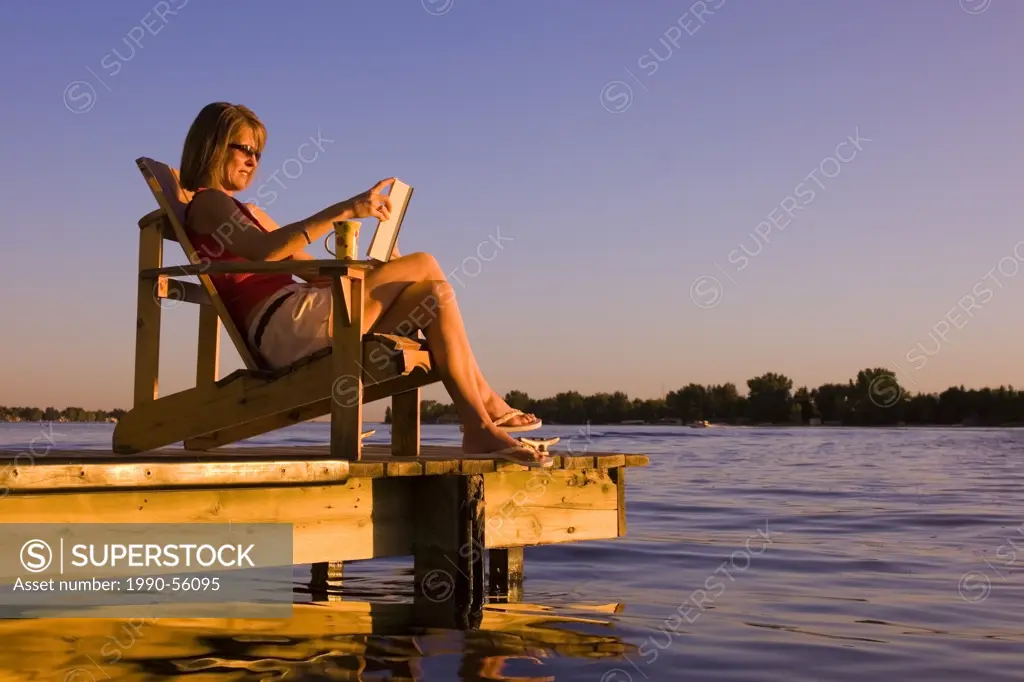 woman relaxing on dock at lake. Alberta, Canada.
