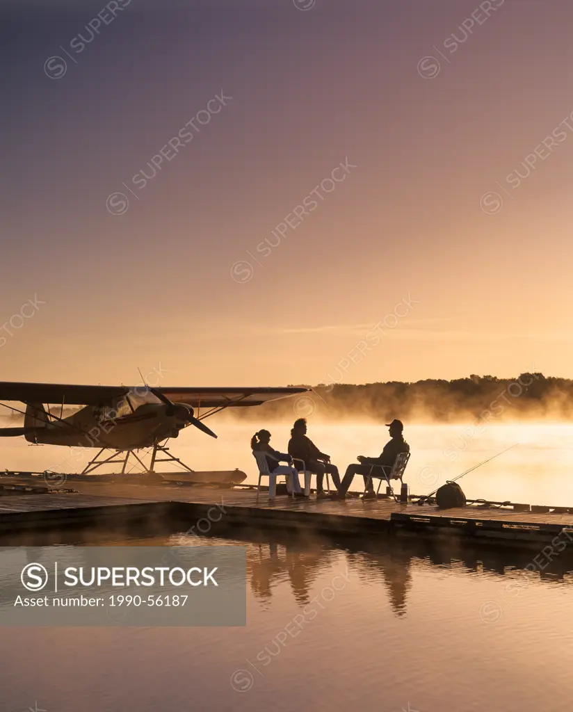 Silhouette of family sitting on float plane dock in the morning, Red River, Manitoba, Canada