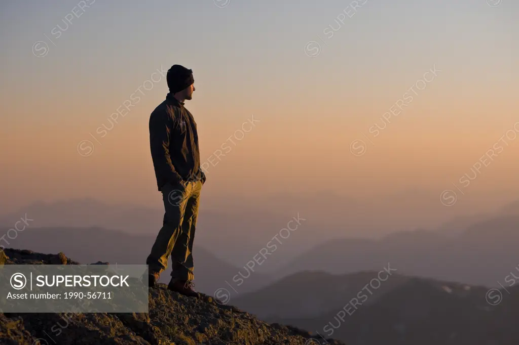 A lone mountain climber stands atop King´s Peak and enjoys the last rays of the setting sun, Strathcona Park, Central Vancouver Island, British Columb...