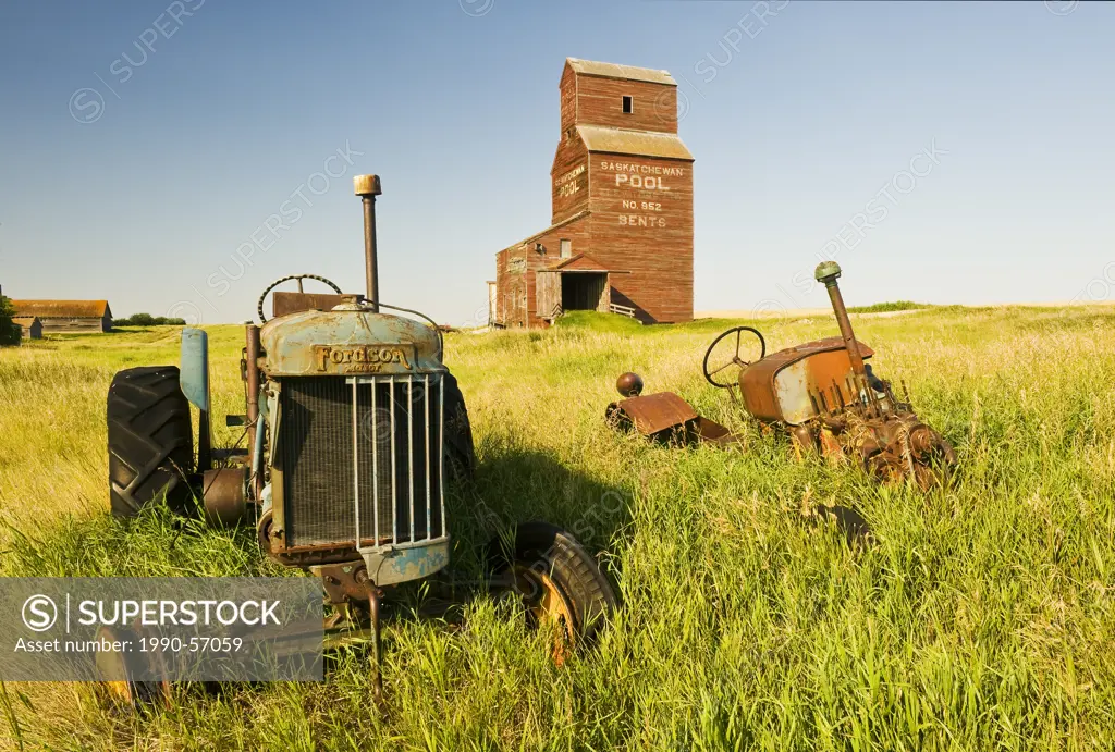 Old tractors with grain elevator in the background, abandoned town of Bents, Saskatchewan, Canada