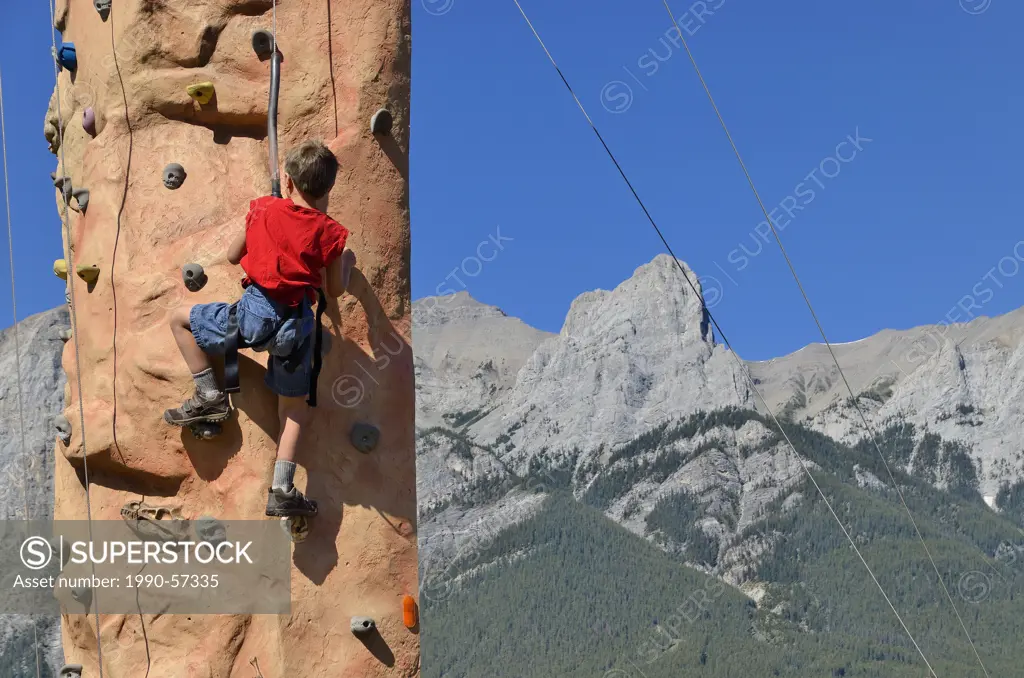 Young boy on climbing wall with mountains in background, Canmore, Alberta, Canada