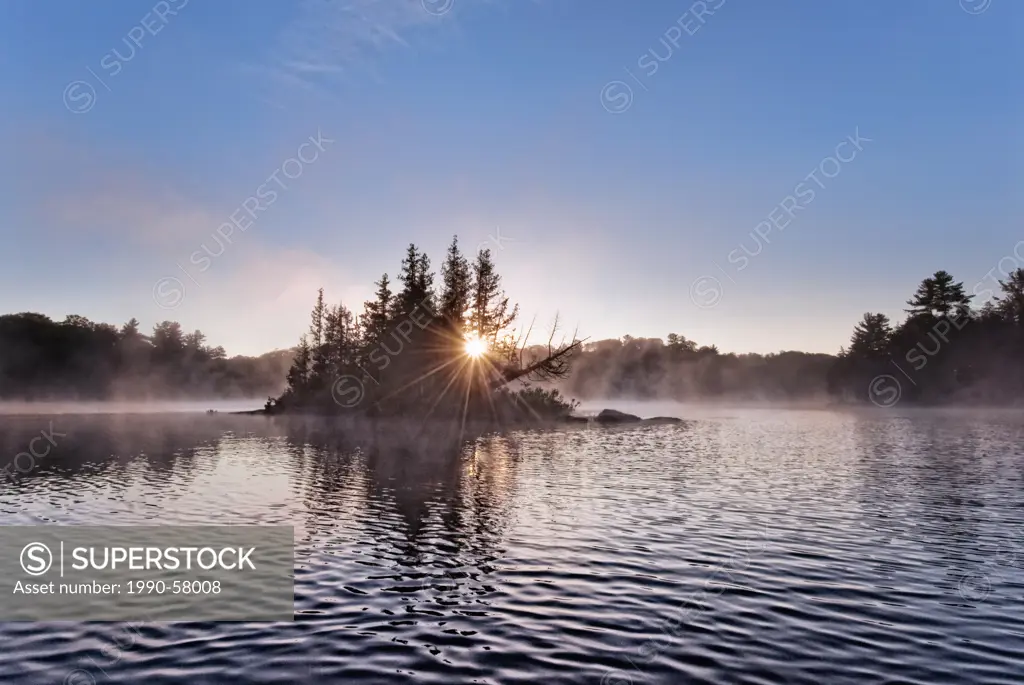 Sunburst and small island in Horseshoe Lake at daybreak in Ontario´s Muskoka region near Parry Sound, Ontario, Canada