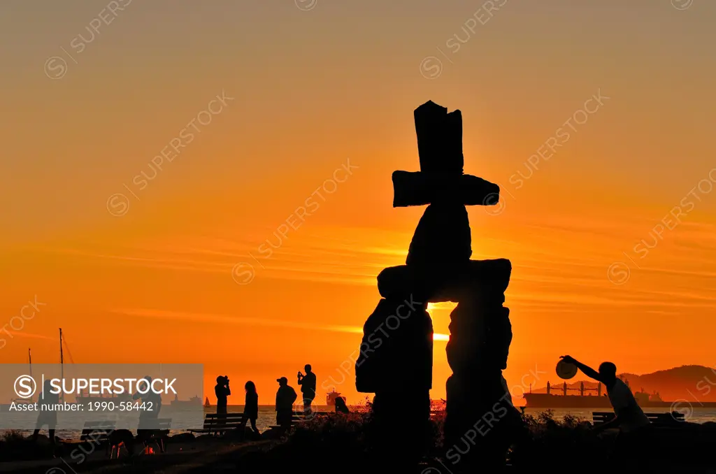 Silhouetted people and Inukshuk at sunset, English Bay, Vancouver, British Columbia, Canada