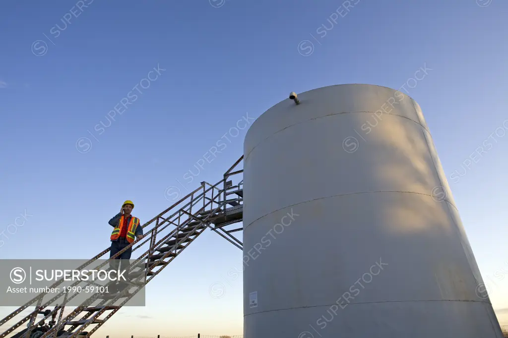 Oil industry worker on storage tank platform talking on phone.