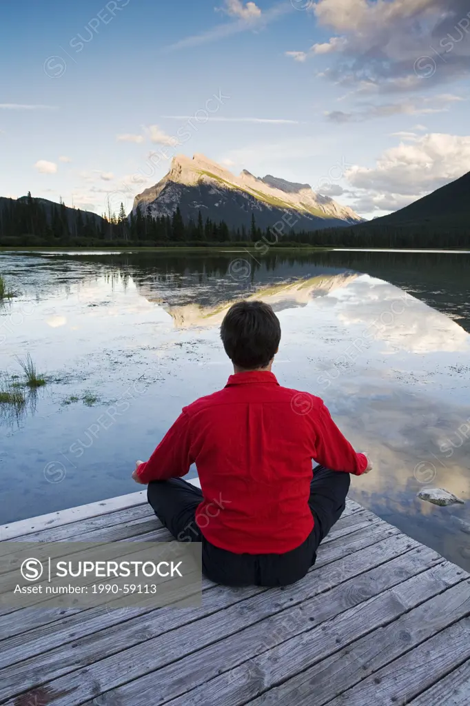 Middle age man meditating on dock at Vermillion Lake, Banff National Park, Alberta, Canada.