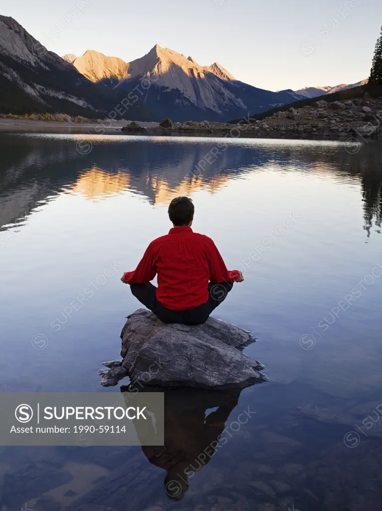Middle age man meditating on rock on Medicine Lake, Jasper National Park, Alberta, Canada.