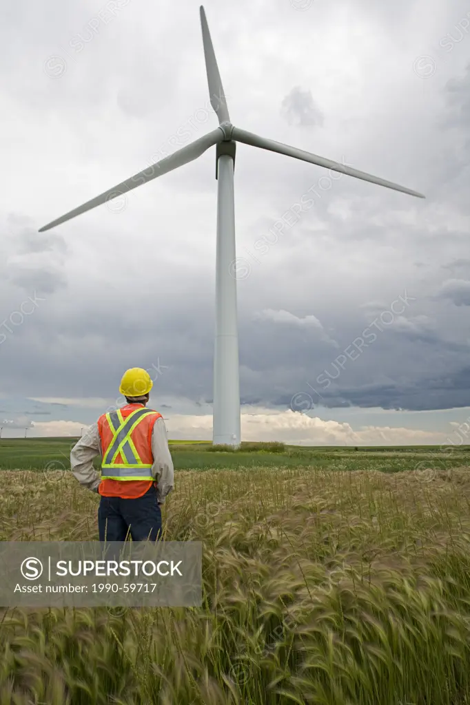 Wind power technician standing next to wind turbine, near Pincher Creek, Alberta.