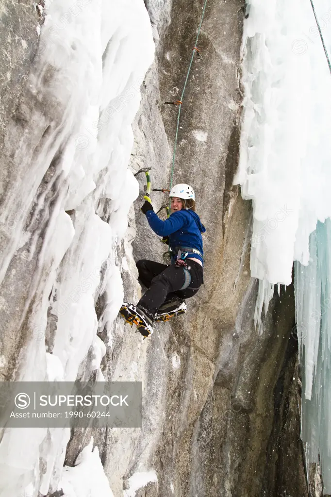 Young woman climbs a mix of ice and rock while ice_climbing in Banff National Park near Banff, Alberta, Canada.