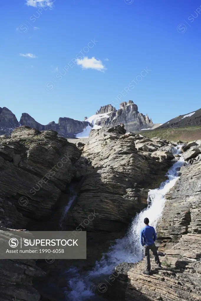 Hiker looking at a waterfall on Dolomite Creek with Dolomite Peak in the background, Banff National Park, Alberta, Canada
