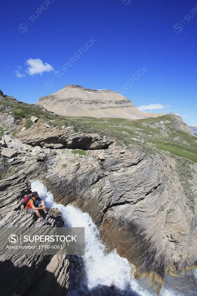 Hiker sitting by a waterfall on Dolomite Creek in the Canadian Rocky Mountains, Banff National Park, Alberta, Canada