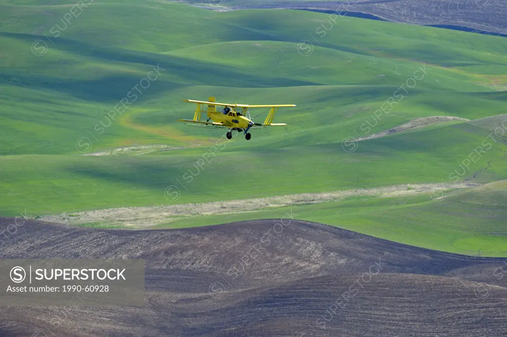 Crop duster aircraft spraying Palouse fields, Washington, USA