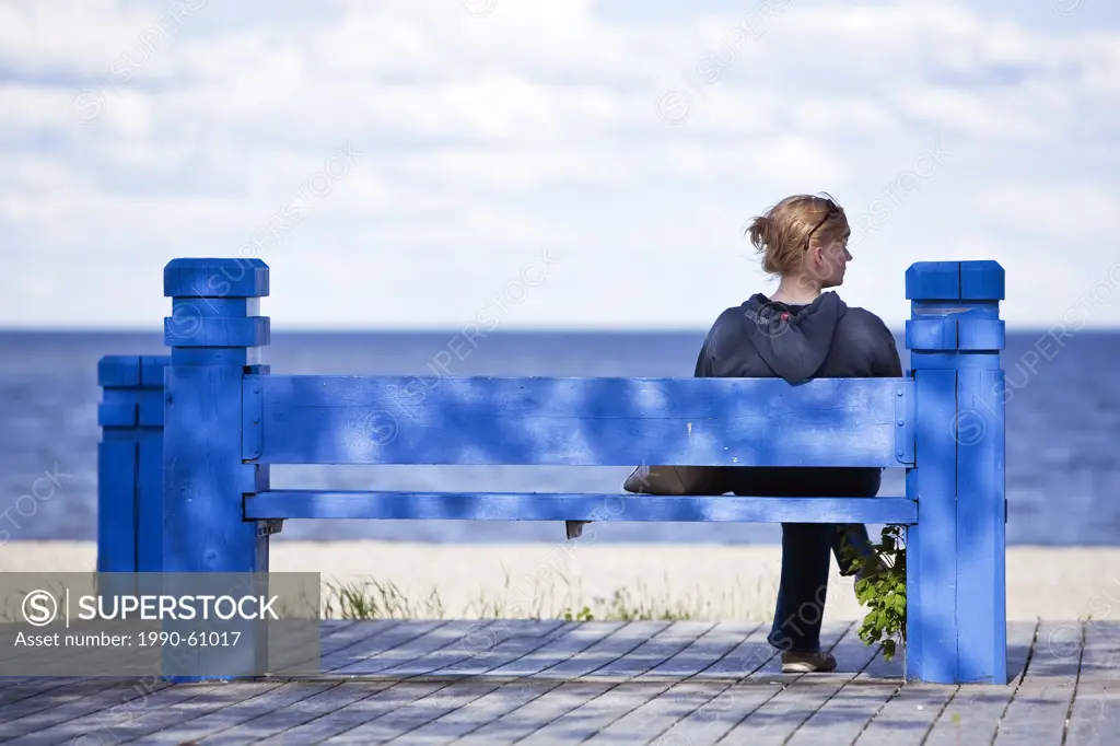 Woman sitting on a blue bench, on Gimli Beach boardwalk, Lake Winnipeg, Gimli, Manitoba, Canada