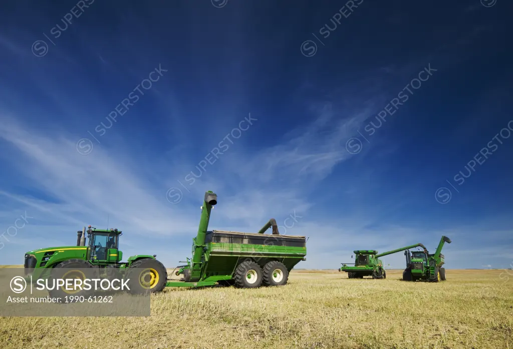 combine harvesters unload into grain wagons during the canola harvest, near Kamsack, Saskatchewan, Canada