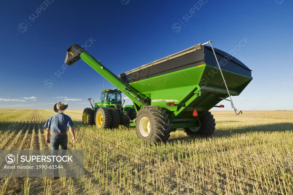 a man next to a tractor and grain wagon during the canola harvest, near Hodgeville, Saskatchewan, Canada