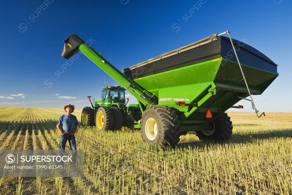 an older man next to a tractor and grain wagon during the canola harvest, near Hodgeville, Saskatchewan, Canada