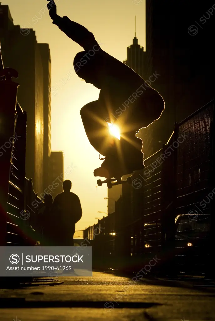 A skateboarder does an ´ollie´ along a street in downtown Toronto at sunset, Ontario, Canada.