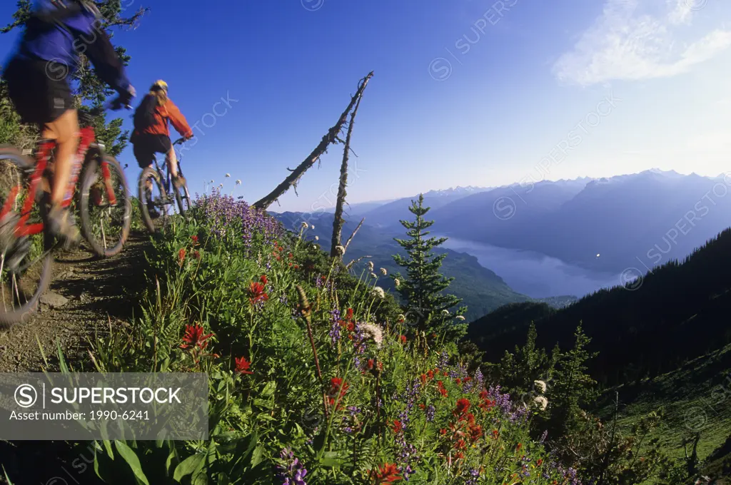 Two woman mountain bikers on Idaho Peak with Valhallas behind, Slocan Valley, Kootenays, British Columbia, Canada