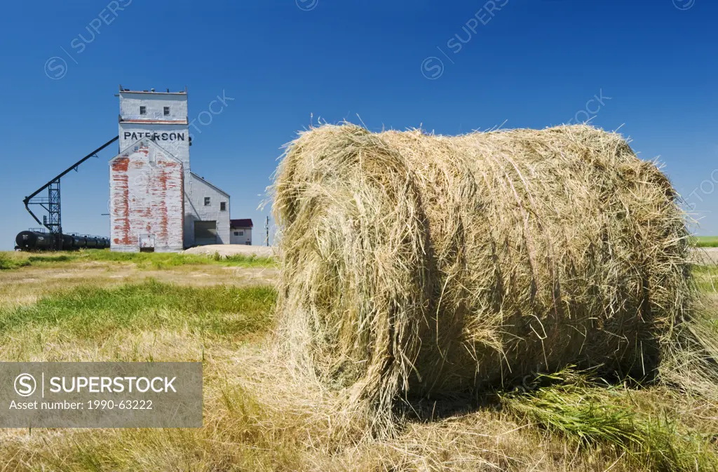field with round hay bale and old grain elevator, Prelate, Saskatchewan, Canada